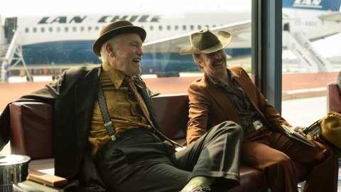 Two men relax and laugh in the departure lounge at an airport,