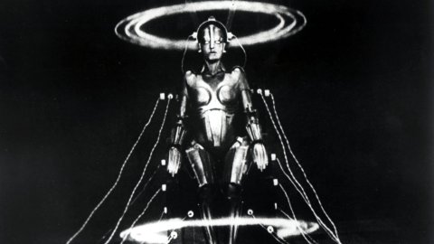A black and white image of a humanoid robot with wires attached in a darkened room