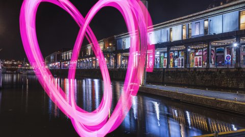 Watershed building at night, shot from the water, with a large pink heart drawn across the whole building.