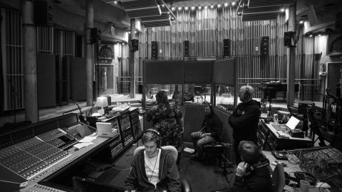 A greyscale still of a large room, filled with audio equipment. 