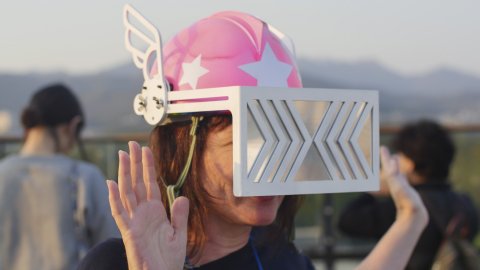 A person wearing a pink helmet with wings on, and a large rectangular viser over their eyes.