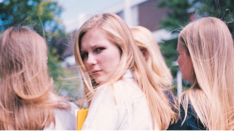 A woman turns to look at the camera, her face quizzical. Three other women walk beside her. 