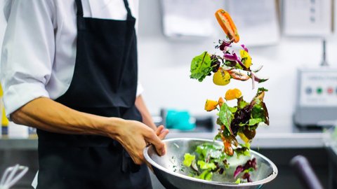 shot of chef's hand tossing a salad into a silver bowl