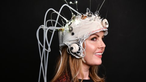 A woman in side profile smiling. She has a headset on her head, with multiple wires protruding from it. 