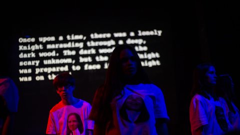 A group of people in a darkened room, illuminated by blue and pink filters.