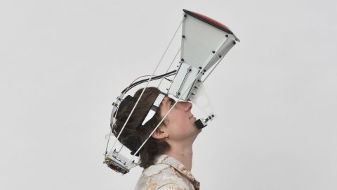 A person wearing a large projector-like device strapped to their face, gazes up.