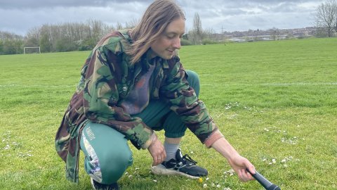 Person crouching down on the grass holding a microphone to the ground. 