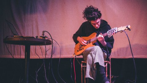 A man sits on a stool, playing a guitar.