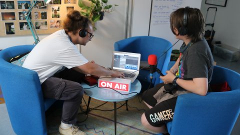 Two young white people wearing headphones connect to a silver macbook air.