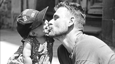 A black and white photo of the artist Andrew Kötting kissing his daughter Eden on the cheek.