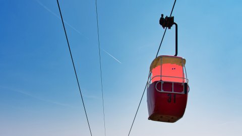 A coral coloured barrel like character sits in a cable car with a beautiful landscape behind it in Llandudno.