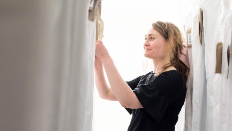 A person wearing a short sleeved black top smiles as she adjusts a garment.