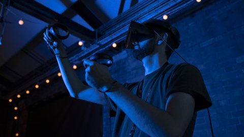Someone in a darkened room wears VR goggles.