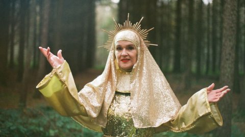 A woman dressed as a golden Virgin Mary poses in a forest.