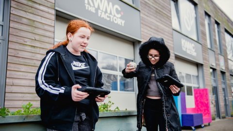 Two young people smiling and working on tablets outside KWMC.