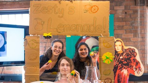 Three participants on the Make Shift Camp 2024 are holding lemons under s sign that reads 'Zesty's Lemonade.'