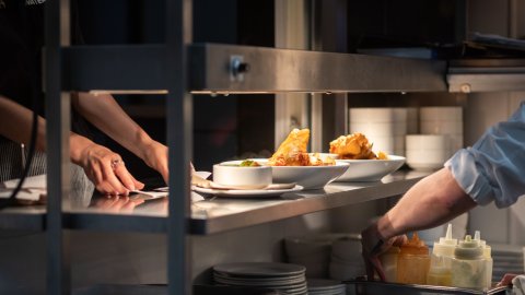 Kitchen staff preparing and organizing plates of fried food and sauces on a metal pass-through counter.