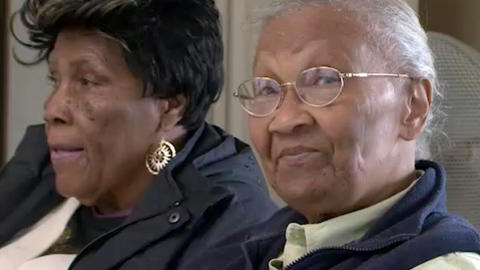 Two older black women, one looking into the camera