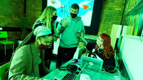 Photo of four people at a creative workshop - 2 sitting at laptops, 2 standing and chatting