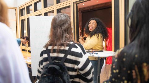 Picture of an artist wearing a yellow jumper explaining their work to a group of onlookers.