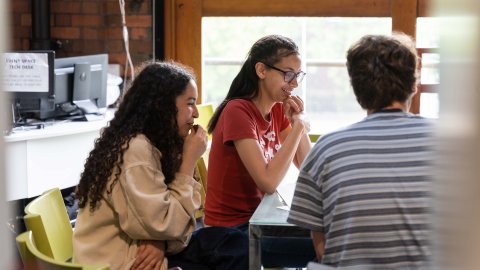 Three young people sitting round a table smiling.