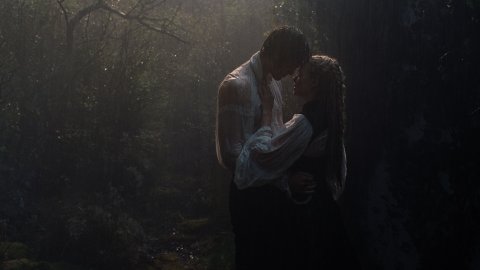 A couple embraces in a misty, rain-soaked forest, surrounded by lush greenery and soft, diffused light.