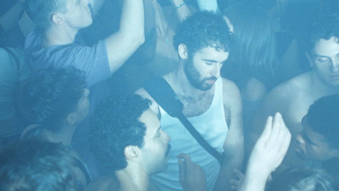 Crowded concert audience dancing and raising their hands under blue stage lighting.
