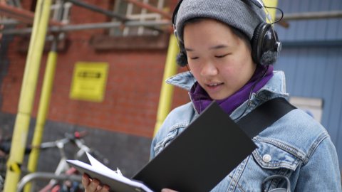 A young person wearing a grey beanie and black headphones is looking through a notebook.