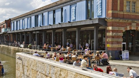Many people sitting in the sun outside the Watershed building on the Bristol harbourside