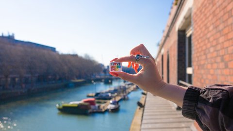 A Club Shed badge is held between a thumb and forefinger. A sunny Bristol Harbourside features in the background.