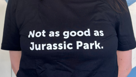 A woman, smiling, is wearing a black t-shirt that reads "Not as good as Jurassic Park."