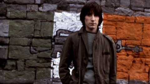 A man stands in front of a wall with graffiti of a flag