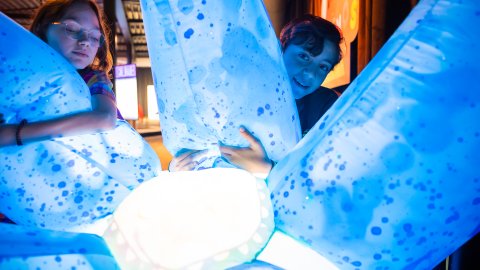 Two children happily squeeze a big blue lit up inflatable thing. Credit: Tom Heuijerjans