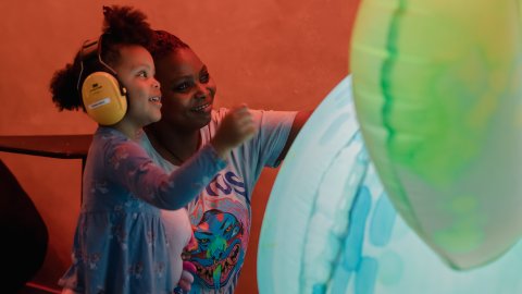 A young Black mum and her child who is wearing ear defenders are intracting with a giant inflatable robot.
