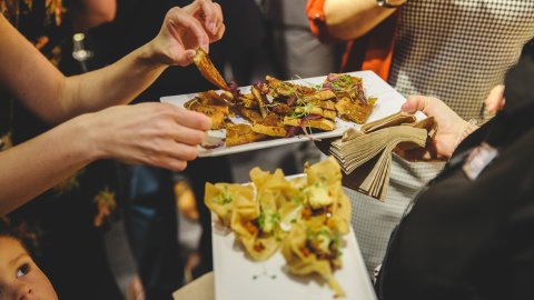A person reaches for a crispy snack from a platter filled with assorted appetisers, featuring garnished bites and fried items.