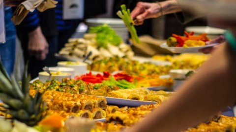 A buffet table filled with a variety of colorful dishes, including fruits, vegetables, and pastries, as guests serve themselves.