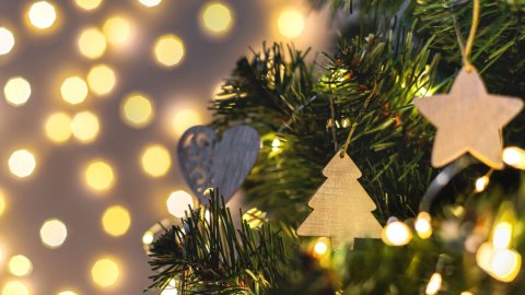 Close-up of a Christmas tree with wooden ornaments, including a star and a tree, against a blurred backdrop of warm, glowing lights.