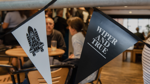 Black and white triangular banners hang in a bar setting, one with a space shuttle graphic, the other with "WIPER AND TRUE" text.