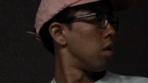 Person wearing a light pink cap and a light-colored shirt, facing sideways against a dark background.