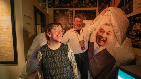 Andrew and Eden Kötting pose beside a large papier-mâché figure of a smiling man in an art-filled room at Undershed.