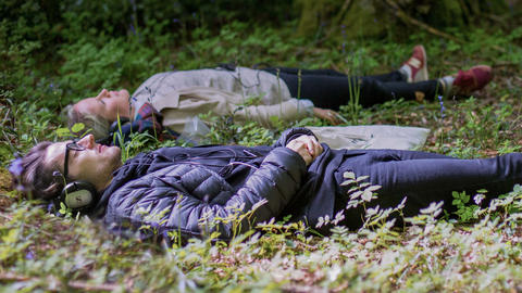 Two people lying down in the woods with headphones on