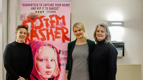 Three women standing with a cinema poster smiling