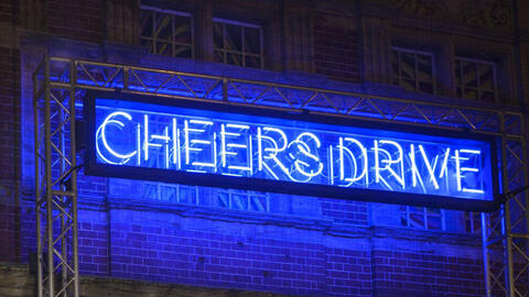 Photo of the exterior of Watershed at night with a large neon sign saying Cheers Drive, as part of Bristol Light Festival