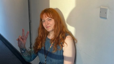 A still of Harriet Taylor, sitting in Watershed's Cinema Corridor.