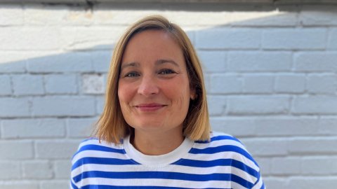 A portrait photograph of a woman looking to the camera, smiling, wearing a blue and white striped t-shirt