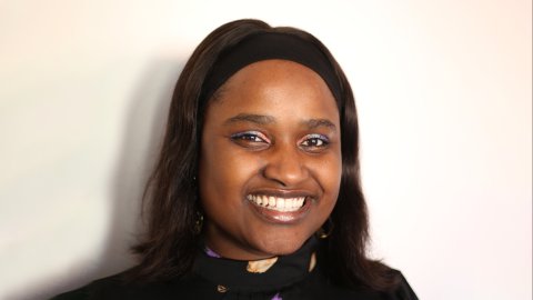 Photograph of Louise Ndibwirende wearing a black top with a colourful pattern on a plain background