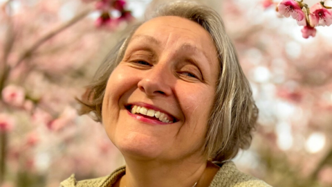 A portrait head shot photograph of Michelle Rumney, a shot woman in their fifties, looking at the camera and smiling