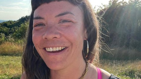 A photo of a woman called Toki Allinson standing in a field on a sunny day, smiling at the camera