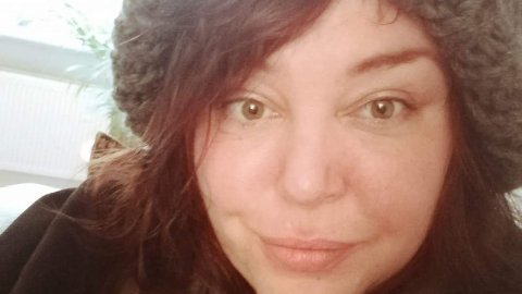 A portrait photo of a white woman looking to the camera, smiling and wearing a grey wooly hat