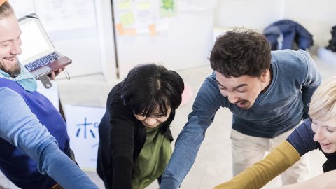 Photo of a group of adults with their hands on top of each other in the middle of a circle